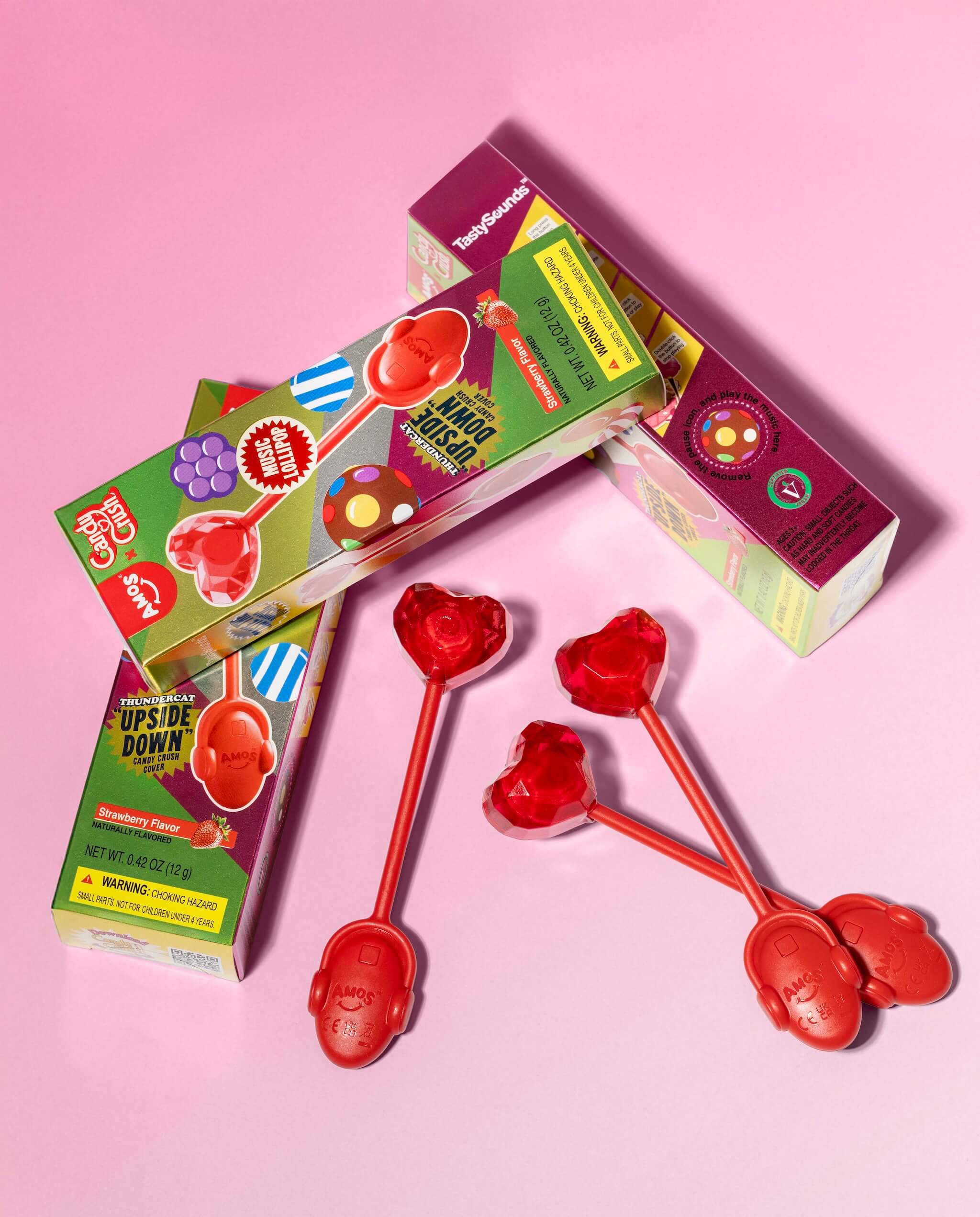 Red heart-shaped lollipop spoons with colorful packaging on a pink background