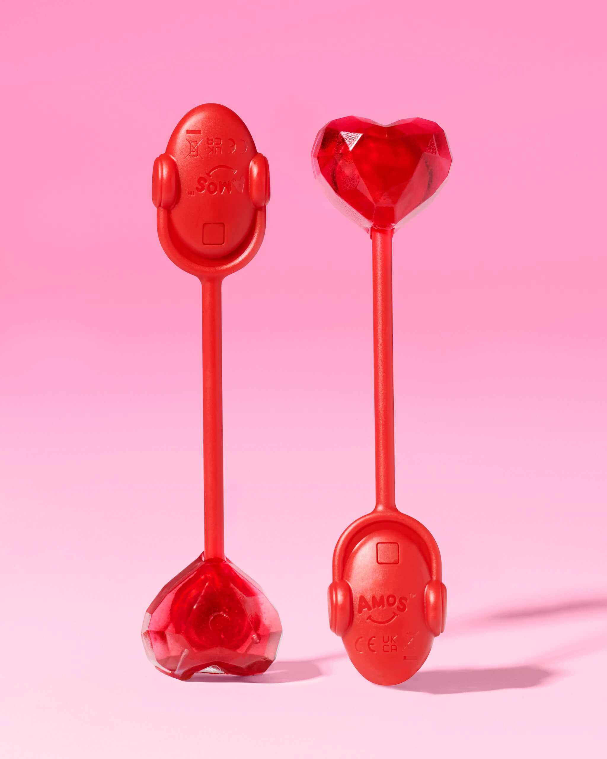 Two red candies with heart and robot head designs on a pink background